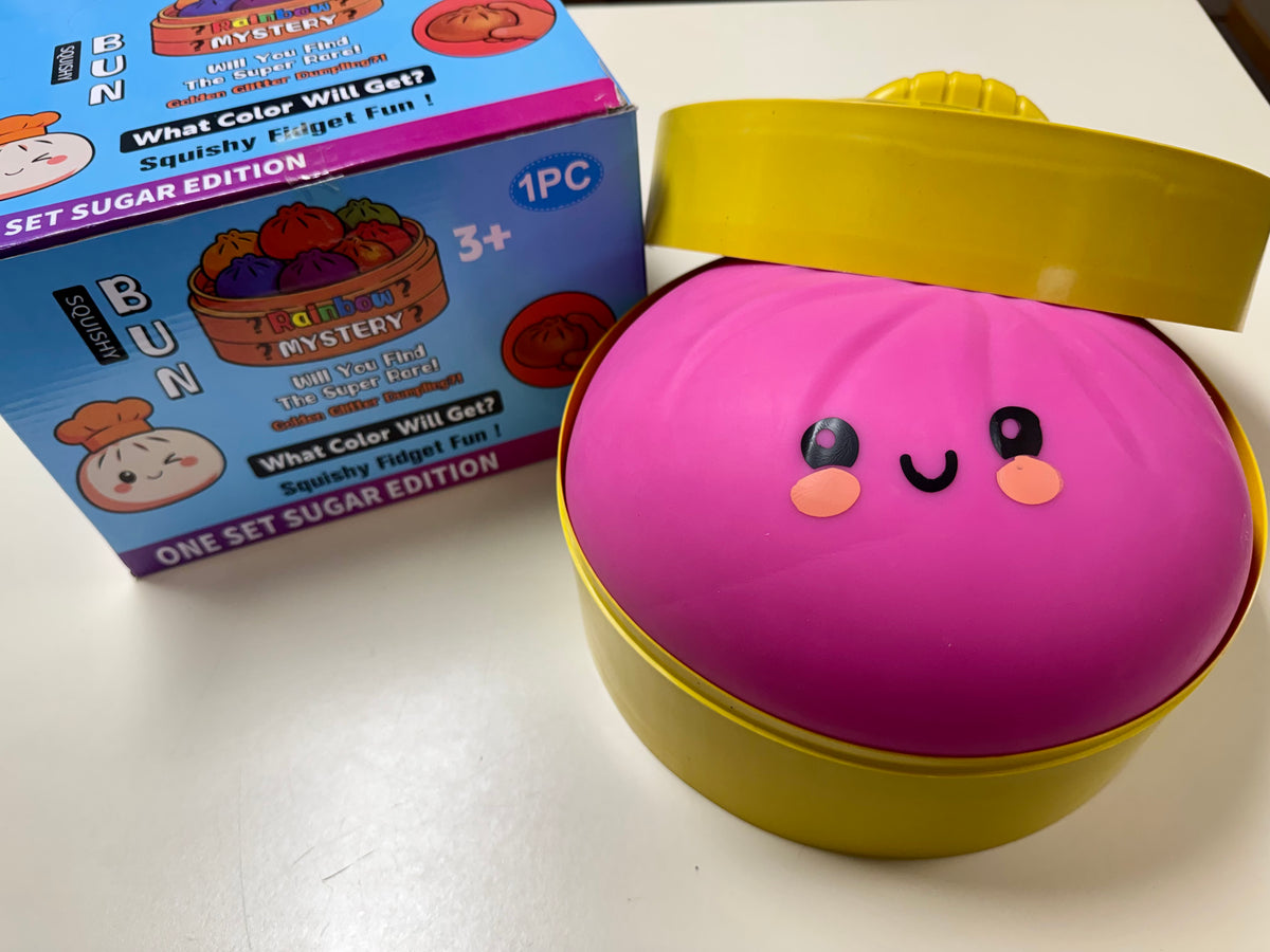 A pink and yellow novelty toy container with a smiling face, shown next to its blue and pink branded retail box on a white surface.