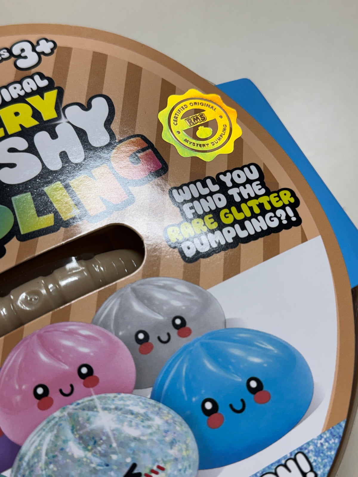 Close-up of official RMS seal for a glitter squishy dumpling surprise toy, and promotional text including 'Will you find the bare glitter dumpling?!'.