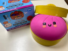 A pink and yellow novelty toy container with a smiling face, shown next to its blue and pink branded retail box on a white surface.